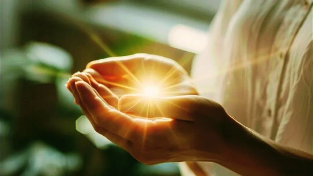 Close-up de mãos em concha com um brilho de luz dourada, durante uma sessão de Reiki.