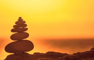 Pedras equilibradas em pirâmide, em silhueta contra o pôr do sol junto ao mar.
